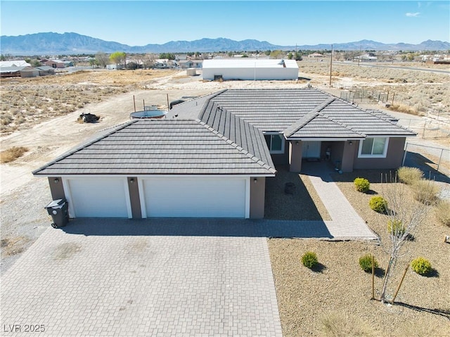 ranch-style house featuring decorative driveway, a mountain view, a tiled roof, and stucco siding