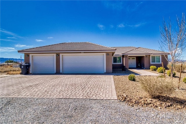 ranch-style house featuring a garage, decorative driveway, a tile roof, and stucco siding