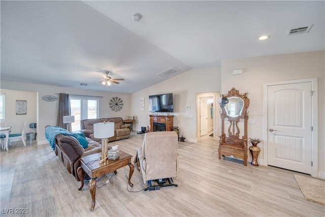 living area featuring lofted ceiling, visible vents, a fireplace, and light wood-style flooring