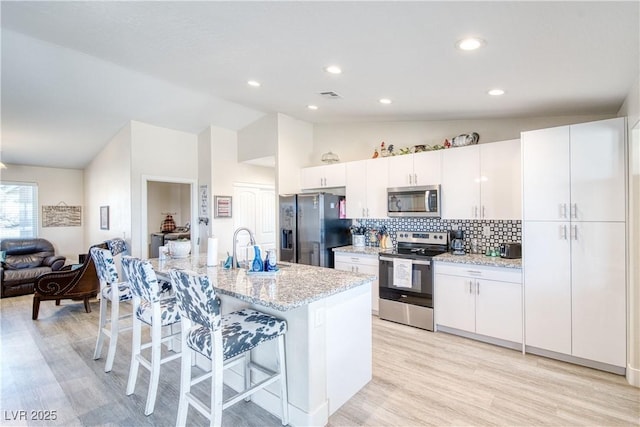 kitchen with visible vents, stainless steel appliances, a kitchen bar, white cabinetry, and a sink