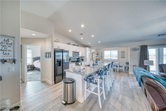 kitchen with a breakfast bar, appliances with stainless steel finishes, open floor plan, white cabinets, and a sink