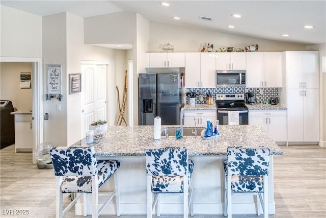 kitchen featuring light wood finished floors, vaulted ceiling, stainless steel appliances, a kitchen bar, and white cabinetry