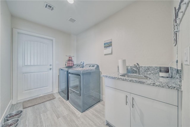 laundry area featuring visible vents, light wood-style flooring, a sink, washer and dryer, and baseboards