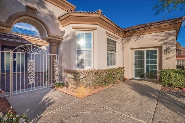 view of exterior entry featuring a gate, fence, a tiled roof, and stucco siding