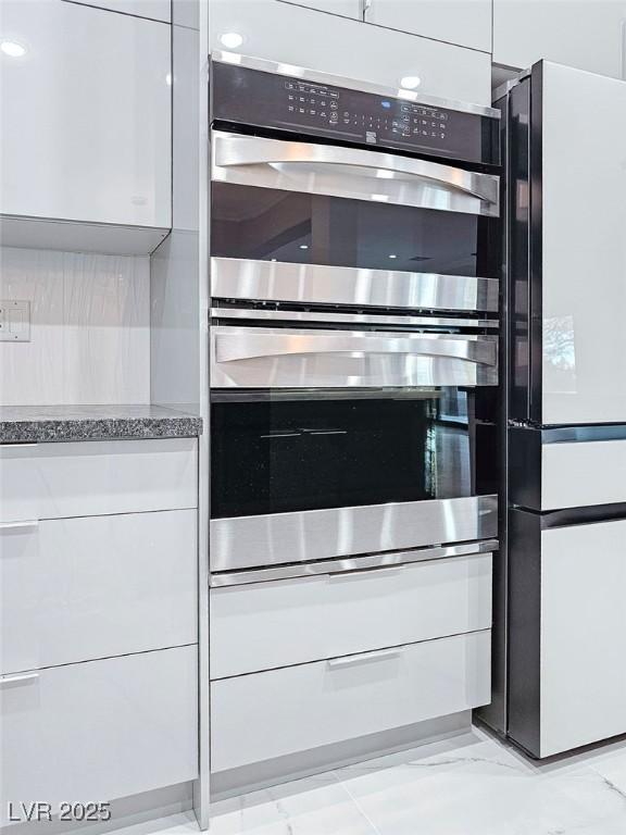 interior details with modern cabinets, light stone counters, freestanding refrigerator, double oven, and white cabinetry