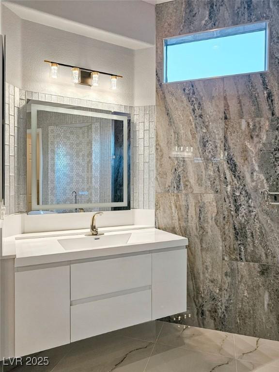 full bathroom with marble finish floor, a shower, vanity, and tile walls