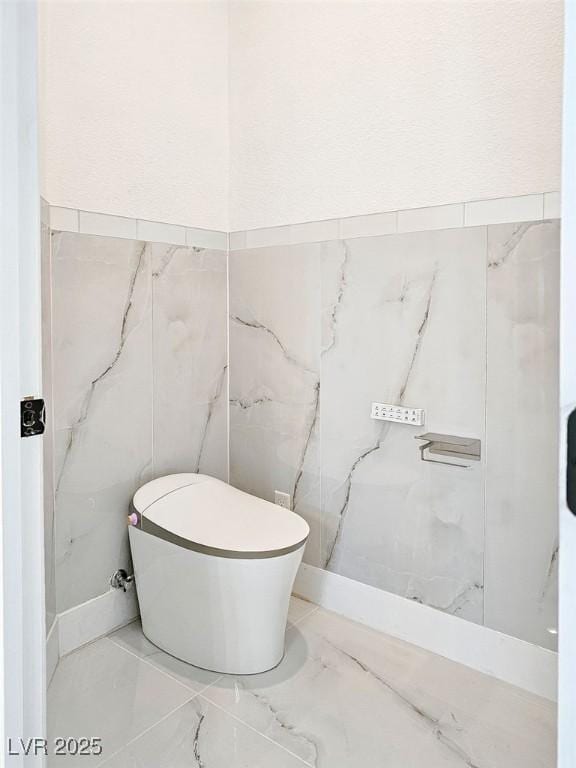 bathroom with marble finish floor, toilet, and tile walls