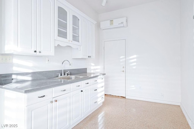 kitchen with glass insert cabinets, a wall unit AC, a sink, and white cabinetry