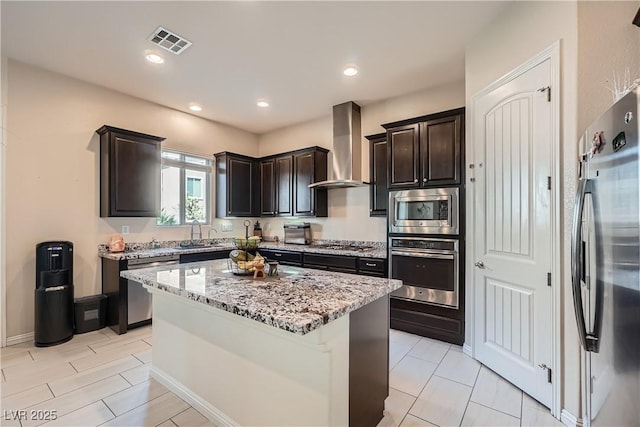 kitchen featuring light stone countertops, visible vents, stainless steel appliances, wall chimney exhaust hood, and a center island