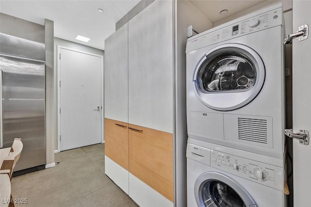 clothes washing area with laundry area, stacked washing maching and dryer, and light tile patterned flooring