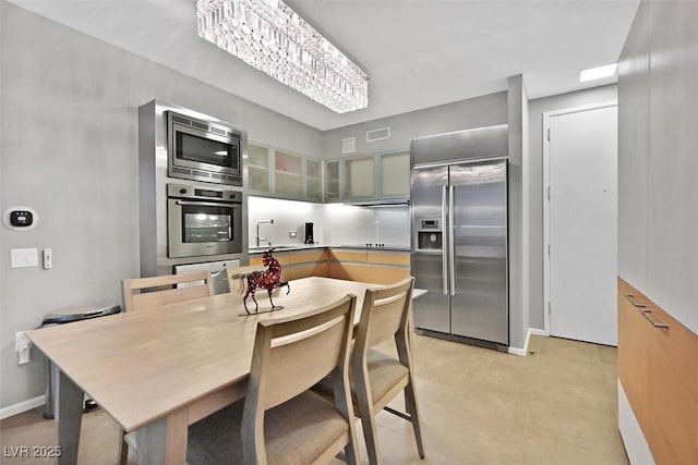 kitchen featuring light tile patterned floors, visible vents, glass insert cabinets, built in appliances, and a sink