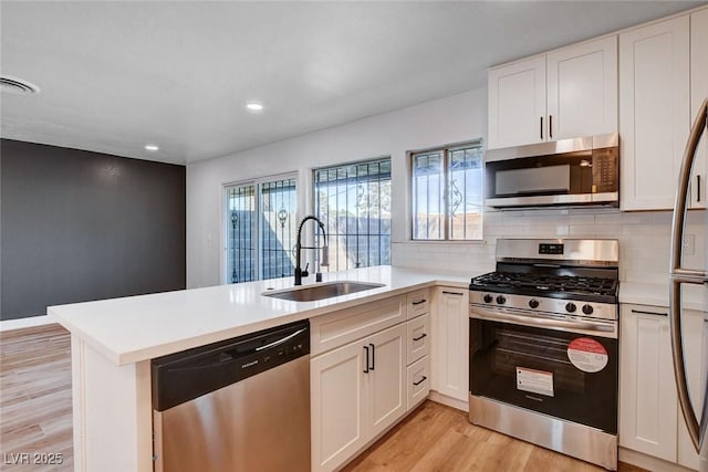 kitchen featuring light countertops, a peninsula, light wood-style floors, stainless steel appliances, and a sink