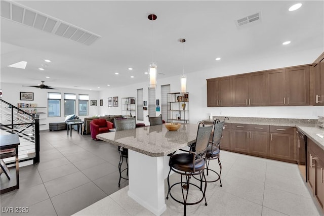 kitchen featuring visible vents, dishwasher, light stone counters, a breakfast bar, and recessed lighting