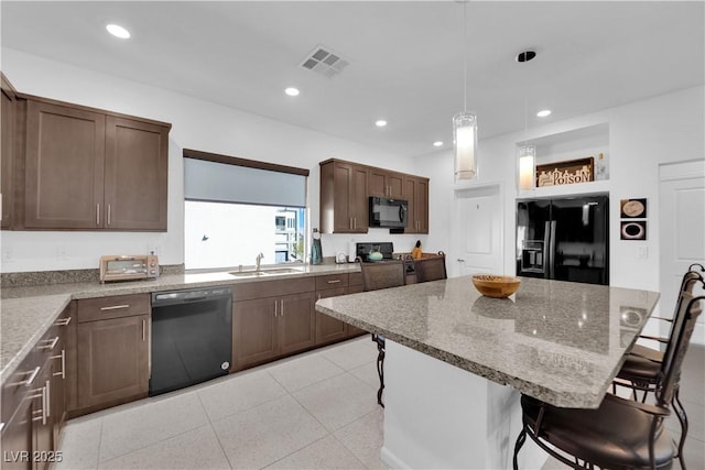 kitchen with visible vents, a sink, black appliances, a kitchen island, and a kitchen bar