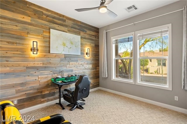 carpeted office space with wood walls, baseboards, visible vents, and ceiling fan