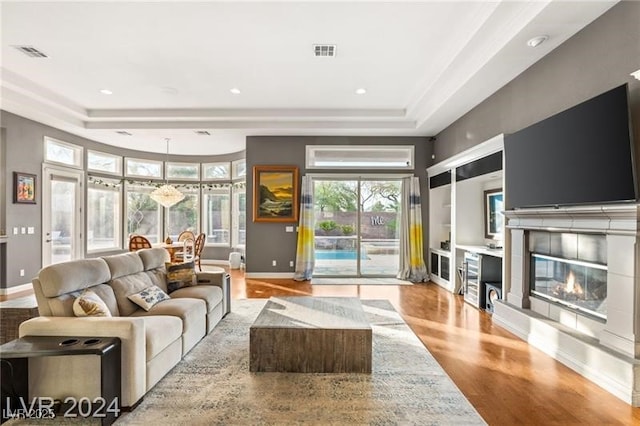 living area featuring a tile fireplace, a raised ceiling, visible vents, and light wood-style flooring