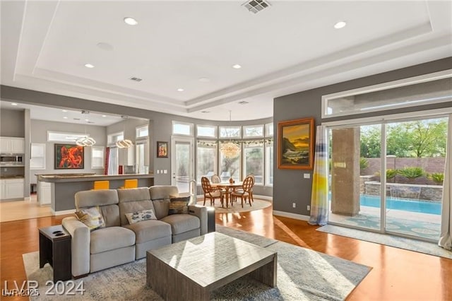 living room with light wood-type flooring, a healthy amount of sunlight, visible vents, and a raised ceiling