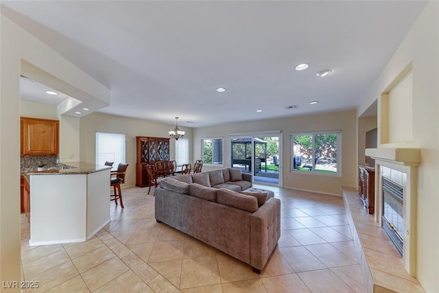 living room with light tile patterned floors, recessed lighting, a tiled fireplace, and an inviting chandelier