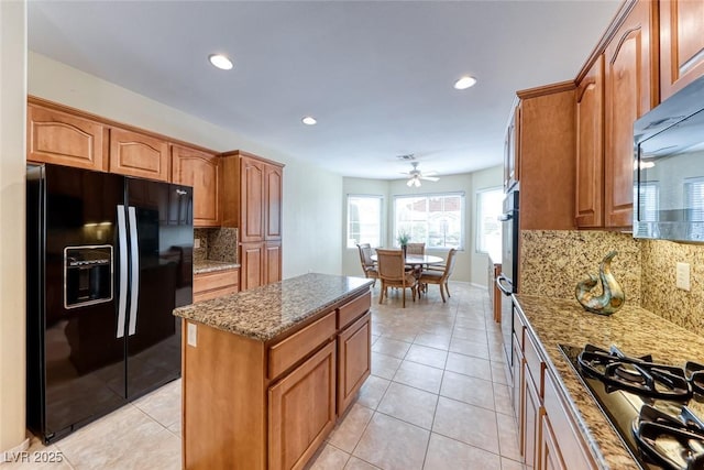 kitchen with stone counters, a center island, black appliances, and light tile patterned floors