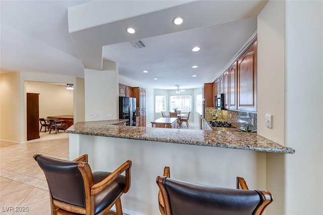 kitchen featuring light tile patterned floors, visible vents, a ceiling fan, black fridge with ice dispenser, and a breakfast bar