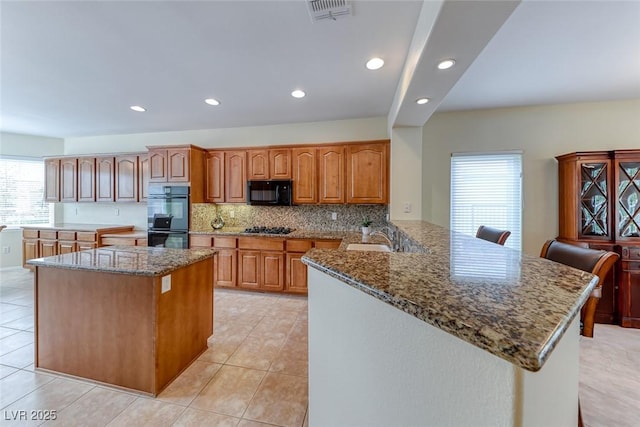 kitchen featuring tasteful backsplash, visible vents, stone counters, black appliances, and a sink