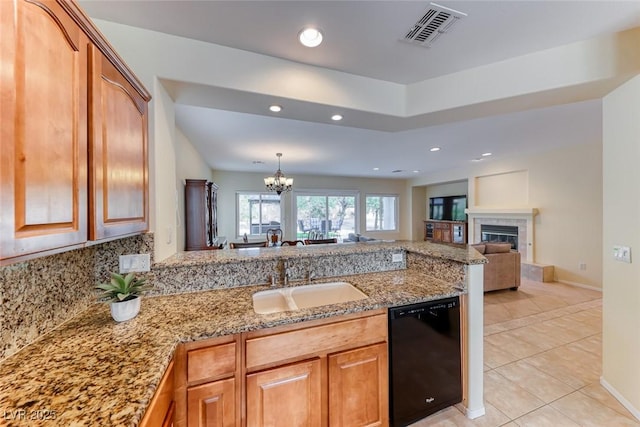 kitchen with light stone counters, visible vents, a glass covered fireplace, a sink, and dishwasher