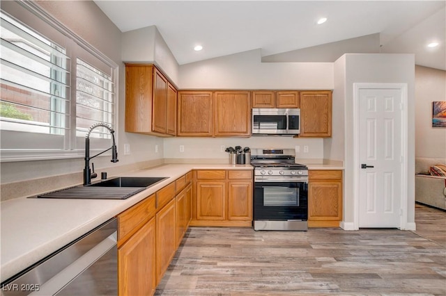 kitchen featuring lofted ceiling, stainless steel appliances, a sink, and light wood-style floors