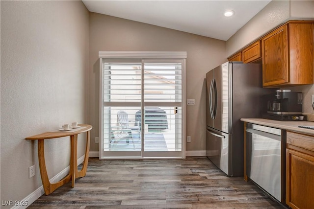 kitchen with lofted ceiling, baseboards, appliances with stainless steel finishes, brown cabinets, and dark wood finished floors