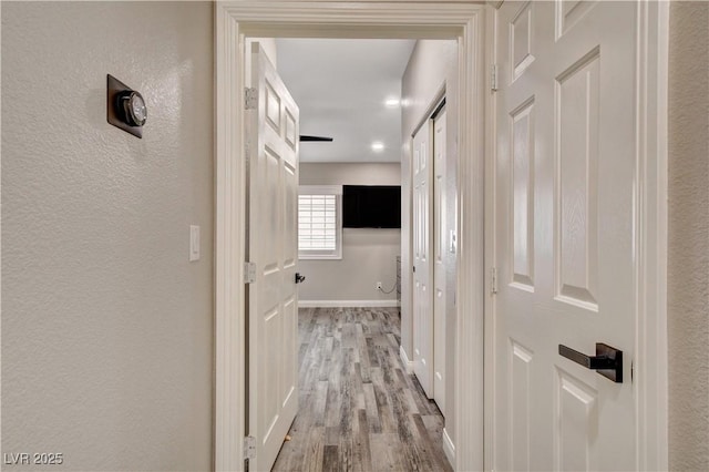 hallway with light wood finished floors, baseboards, and a textured wall