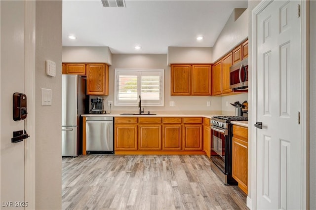 kitchen with brown cabinetry, light wood-style flooring, appliances with stainless steel finishes, light countertops, and a sink