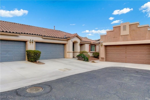 mediterranean / spanish home featuring driveway, a tiled roof, an attached garage, and stucco siding