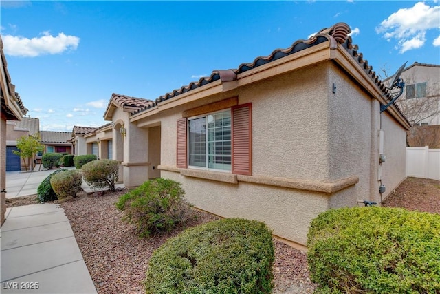 view of side of home with a tiled roof, fence, and stucco siding