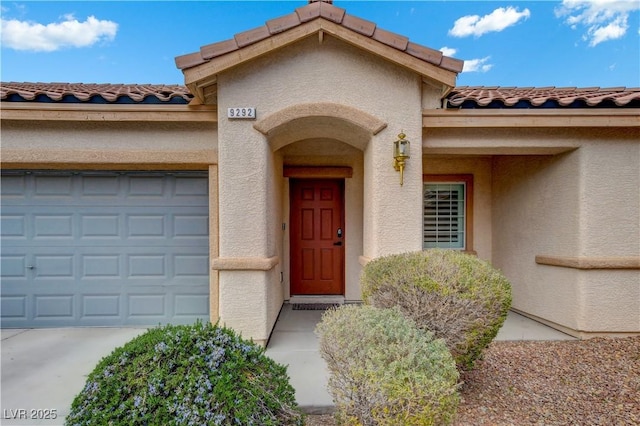 property entrance featuring an attached garage, a tile roof, and stucco siding