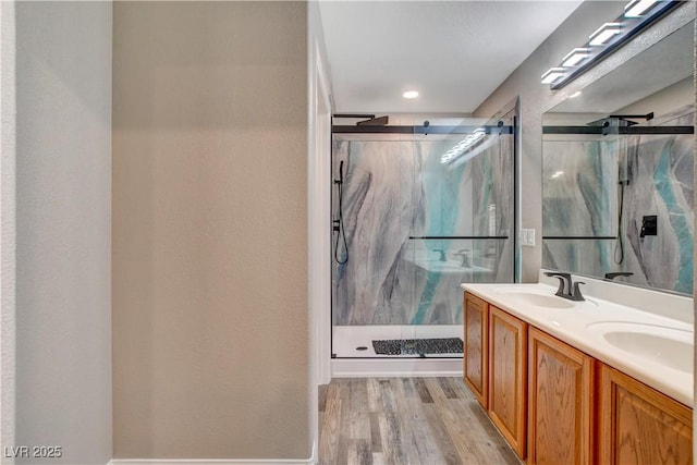 bathroom featuring double vanity, a marble finish shower, a sink, and wood finished floors