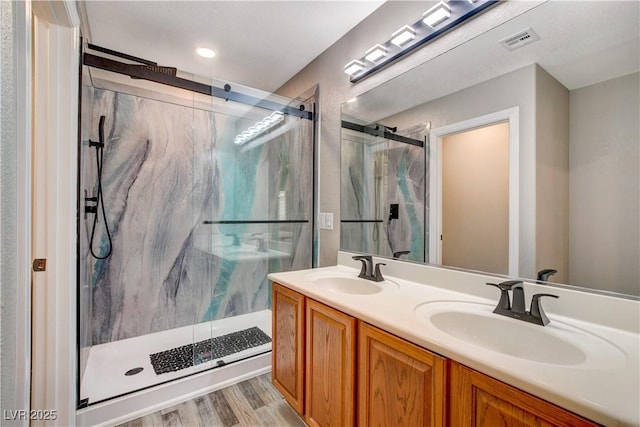 bathroom with visible vents, a sink, a marble finish shower, and double vanity