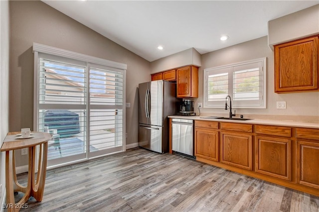 kitchen featuring lofted ceiling, brown cabinets, stainless steel appliances, light wood-style floors, and a sink