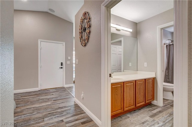 bathroom with toilet, vaulted ceiling, vanity, wood finished floors, and baseboards