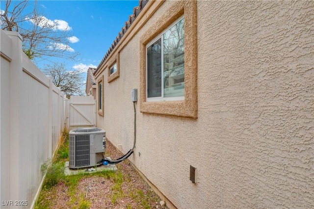 view of home's exterior with a gate, fence, cooling unit, and stucco siding