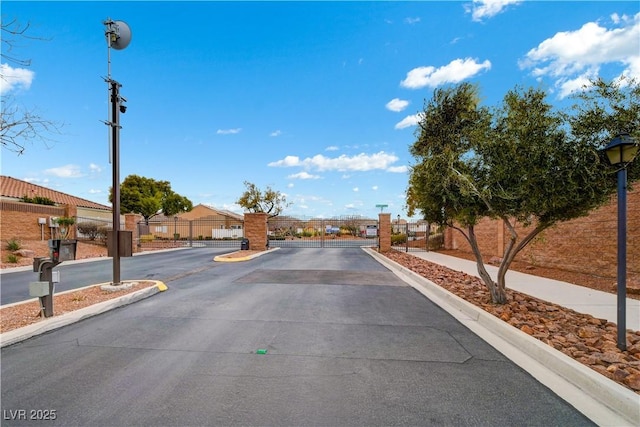 view of street with a gated entry, curbs, a gate, sidewalks, and street lights