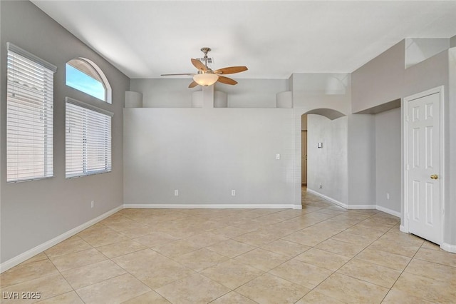 empty room featuring light tile patterned floors, ceiling fan, arched walkways, and baseboards