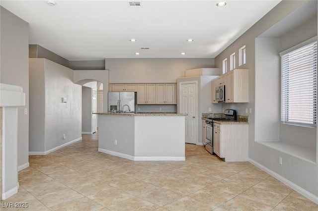 kitchen with arched walkways, a center island with sink, recessed lighting, appliances with stainless steel finishes, and baseboards