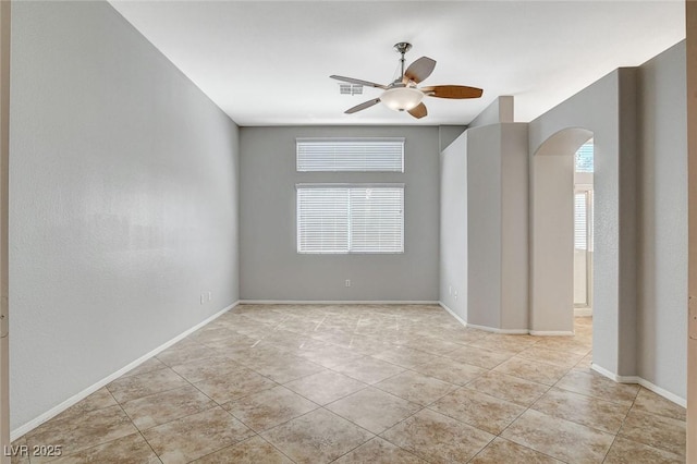 empty room with visible vents, baseboards, arched walkways, and a ceiling fan