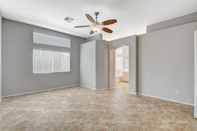 unfurnished room featuring arched walkways, light tile patterned floors, visible vents, ceiling fan, and baseboards