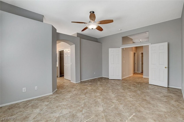 empty room with arched walkways, ceiling fan, baseboards, and light tile patterned floors