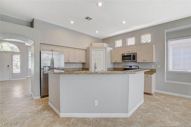 kitchen with arched walkways, light stone counters, a kitchen island, visible vents, and appliances with stainless steel finishes