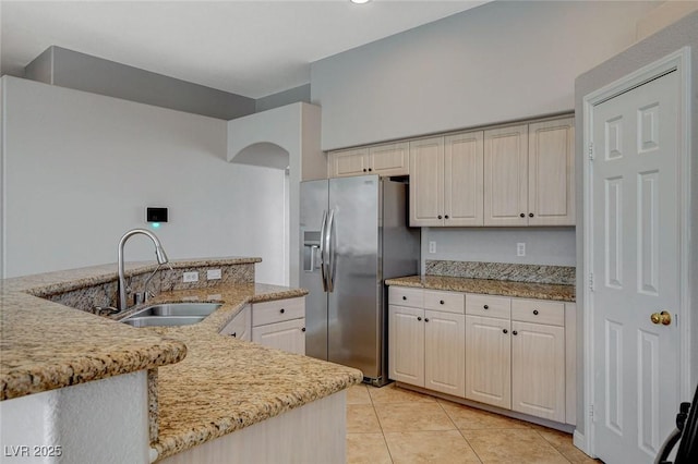 kitchen featuring light tile patterned floors, arched walkways, a sink, stainless steel fridge with ice dispenser, and light stone countertops