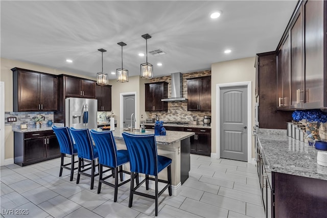 kitchen with a center island with sink, a kitchen bar, visible vents, appliances with stainless steel finishes, and wall chimney exhaust hood