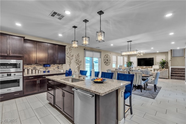 kitchen featuring visible vents, appliances with stainless steel finishes, open floor plan, a kitchen breakfast bar, and a sink