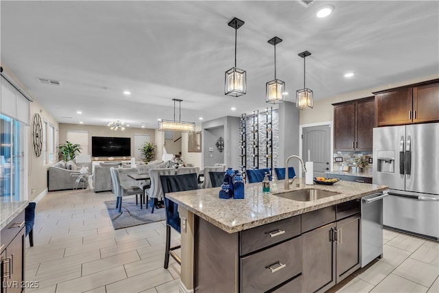 kitchen featuring stainless steel appliances, a sink, visible vents, open floor plan, and dark brown cabinets