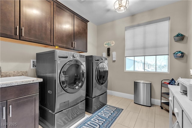 clothes washing area featuring a sink, washing machine and dryer, cabinet space, and baseboards